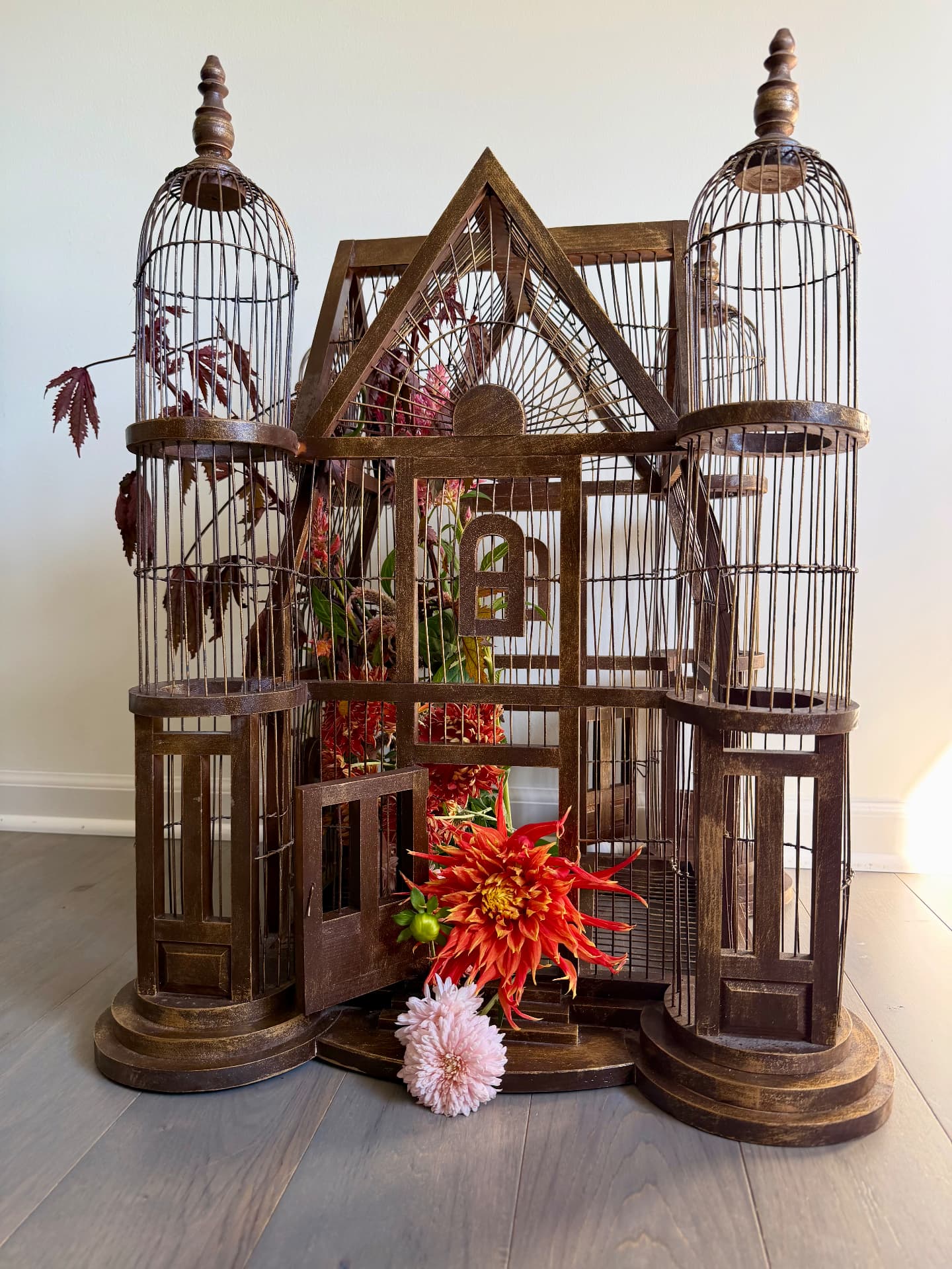 Architectural birdcage with its little door open and autumn flowers spilling out