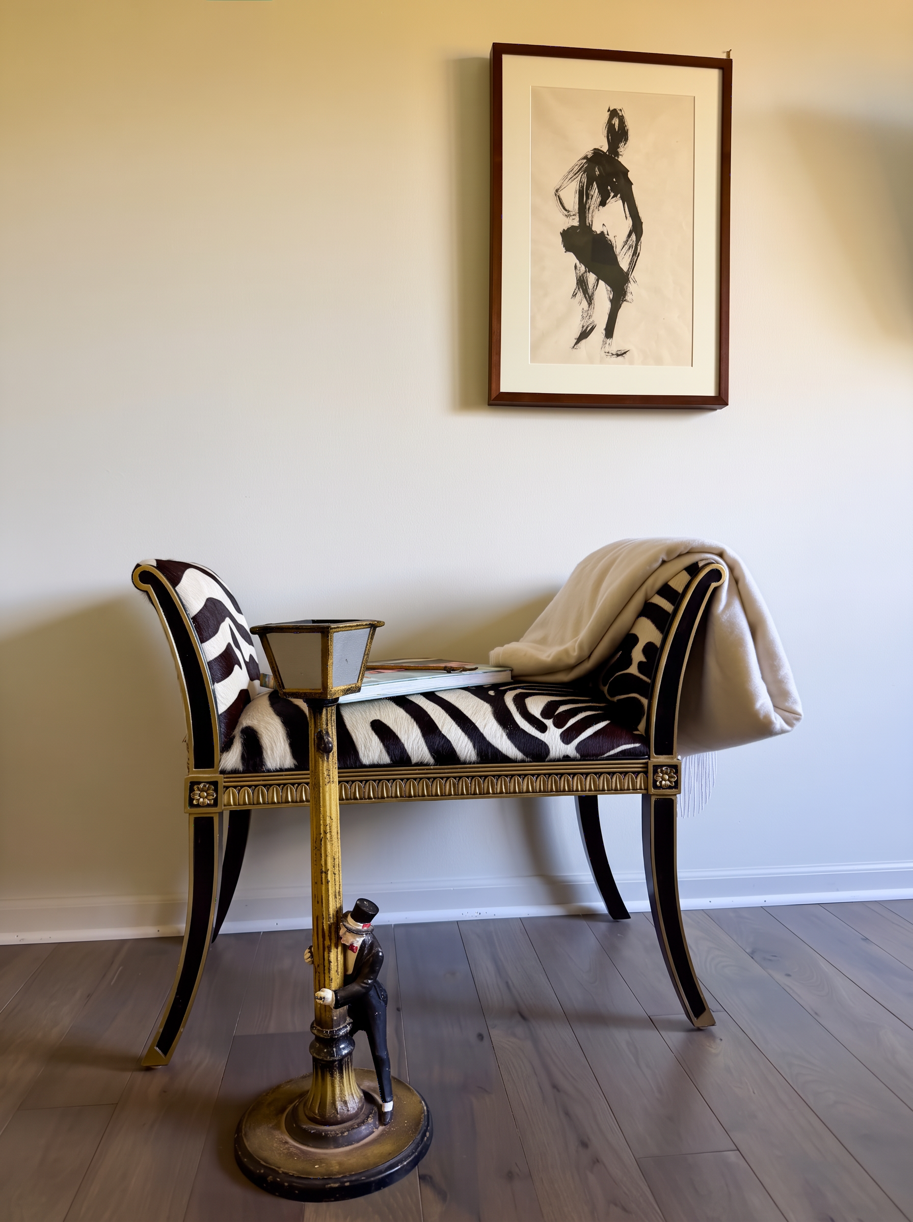Zebra-hide bench beneath an ink figure drawing, with a cast figural ash tray of a gentleman clinging to a lamppost
